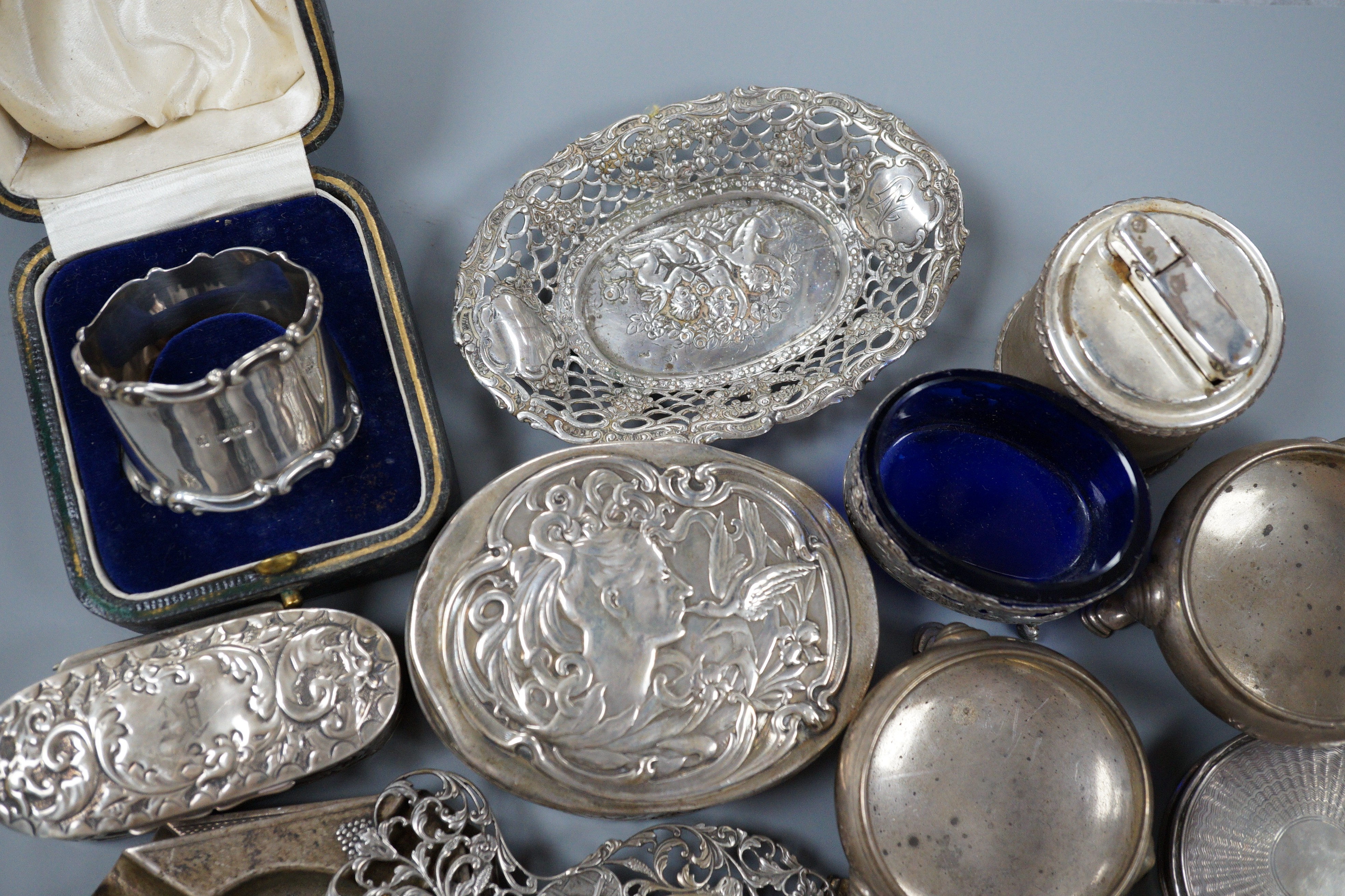 A collection of small silver items including napkin rings, repousse oval boxes, pair of bun salts, two ashtrays and a mounted table lighter, two modern wine labels, small box and three continental white metal items inclu